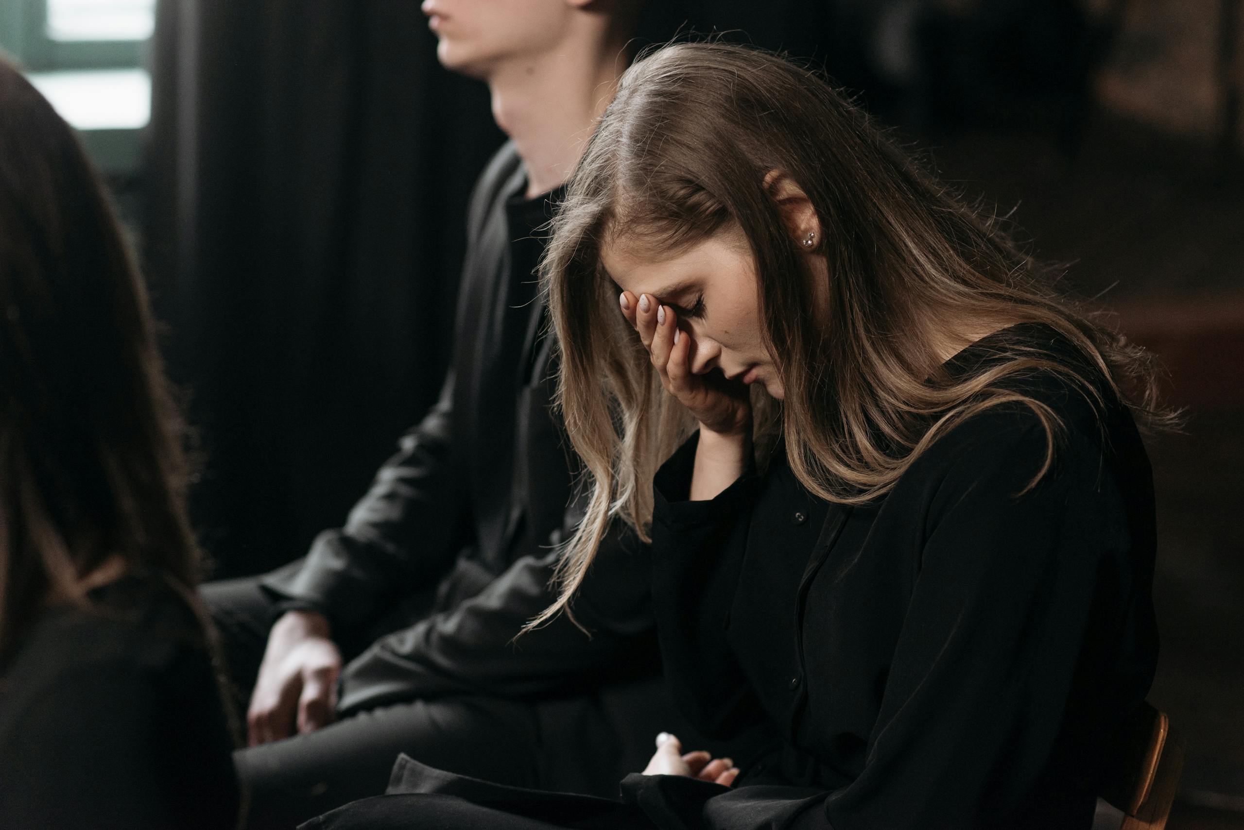 A woman in black clothing expresses sorrow at a funeral, reflecting on loss.